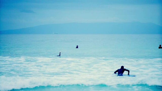 This HD handheld video captures casual surfers at a beach. Although none of the surfers are highly skilled, the scene portrays an approachable and familiar vibe.