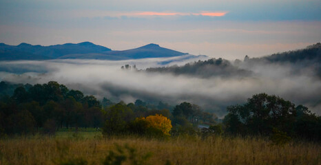 autumn landscape at dusk with thick fog above the village.