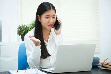 An Asian businesswoman smiles confidently while working at her desk in the office. She diligently analyzes financial data on her laptop, showcasing her expertise and commitment as an accountant