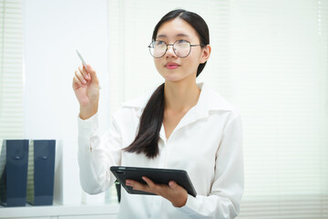 An Asian businesswoman smiles confidently while working at her desk in the office. She diligently analyzes financial data on her laptop, showcasing her expertise and commitment as an accountant