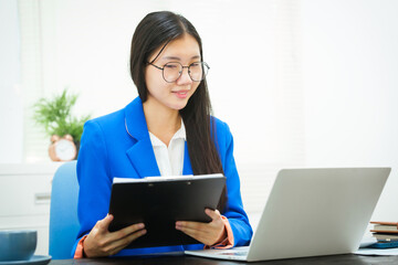 An Asian businesswoman sits at her desk in the office, discussing her work on a business plan. She emphasizes strategic planning, target group identification, and comprehensive business analysis