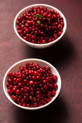 Two bowls of red lingonberries are placed on a burgundy. Top view