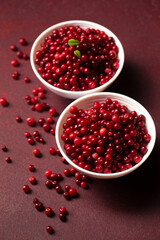 Two bowls of red lingonberries on a burgundy background. close-up