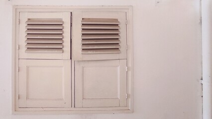 An old white shuttered window against a plain wall, radiating simplicity and vintage charm. Its weathered look tells stories of the past, quietly blending into its surroundings.