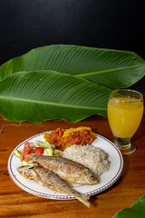 Exquisite Colombian dish with fish, coconut rice, salad and plantain with orange juice on a wooden table. Colombian gastronomy, typical dish.