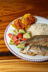 Exquisite Colombian dish with fish, coconut rice, salad and plantain with orange juice on a wooden table. Colombian gastronomy, typical dish.