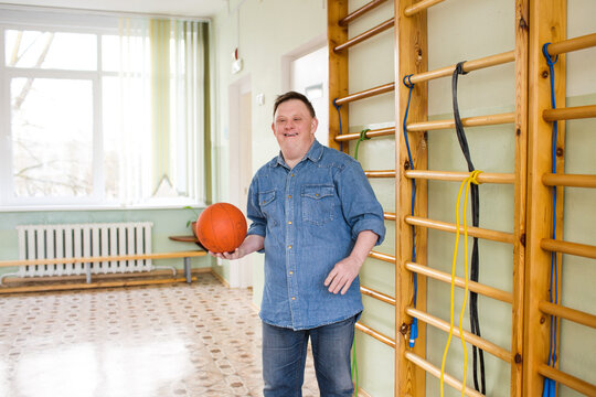 A young man with Down syndrome is holding a basketball and smiling brightly, showing his love for sports and a positive attitude.