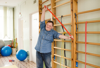 A young man with Down syndrome is stretching with a red pole in a gymnasium. He is smiling and looks happy