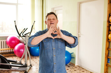 A man with Down syndrome is making a heart shape with his hands in a gymnasium.