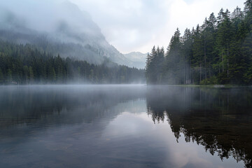 Fototapeta premium A misty mountain range is reflected in the calm lake