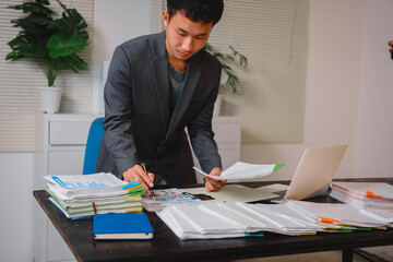 A businessman sits at his desk, working late into the night on his laptop. He reviews documents carefully, showcasing commitment and diligence as he works overtime to meet deadlines