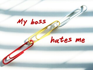 Office paper clips on white background with text written My boss hates me - feeling you are...