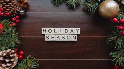 A wooden background with pine branches, red berries, and ornaments on the sides. In the center, the phrase HOLIDAY SEASON is spelled out with white letter tiles.