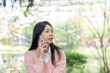 A long-haired Taiwanese woman in her 20s wearing a pink sweater talks on a smartphone while sitting...
