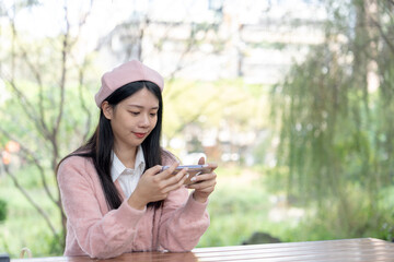 A long-haired Taiwanese woman in her 20s wearing pink sweater and beret operates smartphone while...