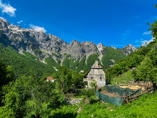 Remote rustic farm house nestled amidst alpine pine forest surrounded by majestic mountain peaks of...