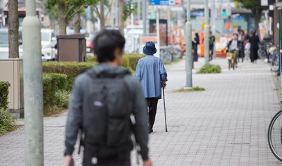 秋の昼の繁華街の道路で歩くシニア女性と人々の姿