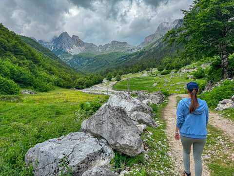 Hiker woman on scenic hiking trail from Kukaj to Maja Jezerce in Valbone Valley National Park, Albania. Majestic cloud covered mountain peaks Albanian Alps (Accursed Mountains). Forest covered slopes
