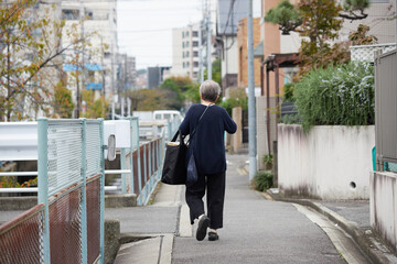 秋の昼の住宅地で歩く一人のシニア女性の姿