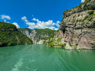 Scenic ferry boat tour on Lake Koman reservoir on Drin river surrounded by forested steep hills,...