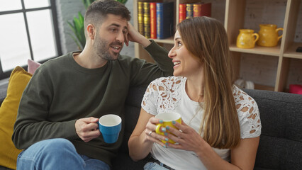 A smiling woman and man enjoy a cozy moment with coffee mugs on a sofa in a stylish living room.