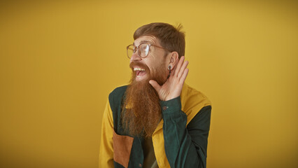 Bearded redhead man smiles and listens over yellow isolated background