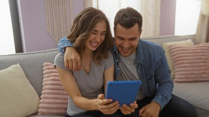 Smiling man and woman sitting together on a cozy couch in their living room, enjoying a moment while looking at a tablet