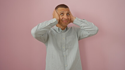 Handsome man covering his ears with his hands against a pink background looking upwards in...