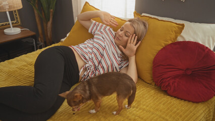 A young blonde woman resting on a bed in a cozy bedroom with her pet chihuahua nearby, creating a...