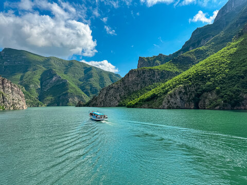 Scenic ferry boat tour on Lake Koman reservoir on Drin river surrounded by forested steep hills, cliffs and majestic rugged mountain ranges of Albanian Alps. Panoramic view along Albanian Fjords. Awe