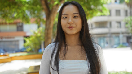 Young, beautiful, chinese woman standing outdoors in an urban park setting with a city background.