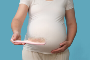 Problems with hair loss during pregnancy, isolated on a studio blue background. A pregnant woman...