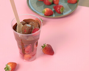 Whole fresh strawberries covered with melted liquid chocolate in cup. Sweet food, dessert on pink background. 