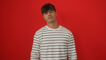 Handsome young hispanic man in a striped shirt against a vibrant red background, showcasing a casual and stylish look.