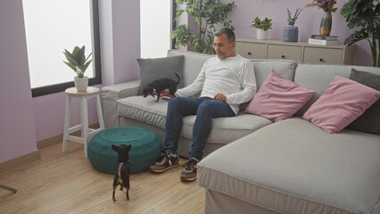 Middle age hispanic man sitting in a living room with two chihuahuas and plants around.