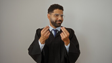 Young hispanic man gesturing money sign while wearing glasses and graduation gown over white background with confident expression