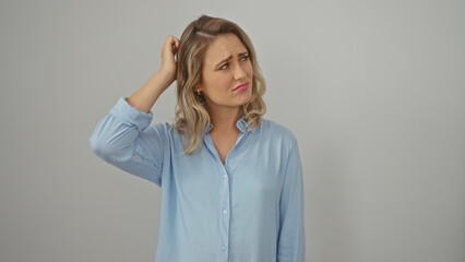 Puzzled young blonde woman in blue shirt with a white background expressing doubt and uncertainty.