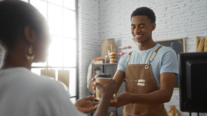 Worker handing coffee to customer in bakery shop with bread and pastries in the background, smiling, indoors, exchanging item, wearing apron, side view