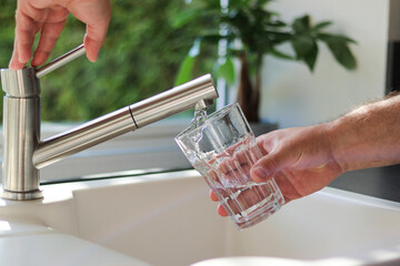Close up of male hands pouring tap water into a glass in the kitchen