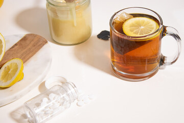Hot tea with fresh lemon and honey, a bottle with white pills on white table