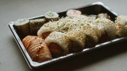 Sushi platter with various rolls and nigiri on black tray placed on concrete surface showcasing fresh and appetizing japanese cuisine.