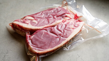Vacuum-sealed raw beef steaks in transparent plastic packaging on a gray countertop indicating freshness and preservation for extended shelf life.