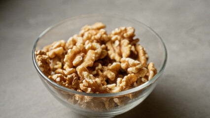 Clear glass bowl filled with fresh, crunchy walnuts on a light gray background, perfect for healthy snack and nutrition concepts