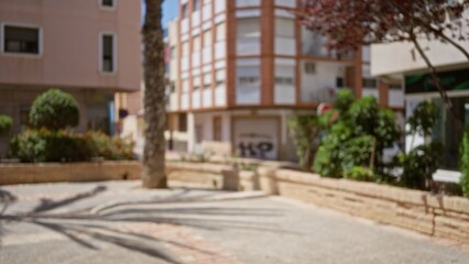 Defocused view of an outdoor urban area with blurred buildings, trees, and plants under bright sunlight, depicting a typical city environment.