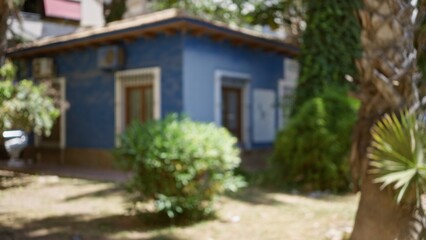 Fototapeta premium Blurred view of a small blue house with greenery in an outdoor setting during daytime with defocused plants and trees surrounding the area