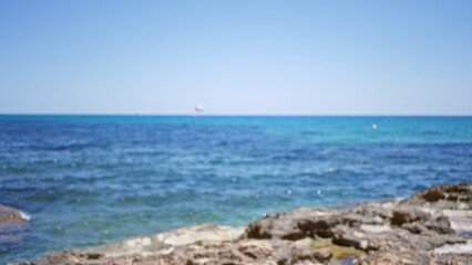 Blurred seascape with defocused horizon and rocky coastline under clear blue sky