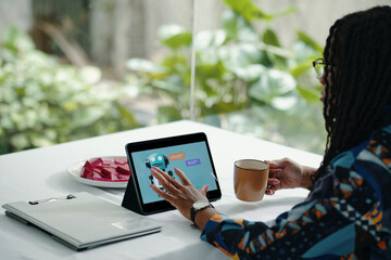 Person sitting at table, interacting with tablet while holding coffee cup, surrounded by documents...