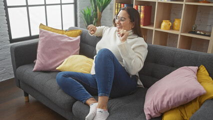 Obraz premium Hispanic woman relaxing on couch in cozy living room interior with colorful cushions.