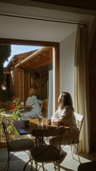 Woman sitting indoors in a bright cafÃ©, enjoying a sunny view through large windows, adorned with simple decor, while savoring a hot drink in a relaxed and cozy ambiance