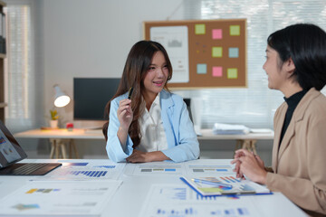 Two Asian businesswomen use laptops and smartphones in an open space office. Business concept. Data analysis, roadmap, marketing, accounting, auditing.